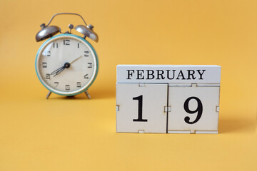 Calendar for February 19: cubes with the number 19 and the name of the month, alarm clock on a yellow background