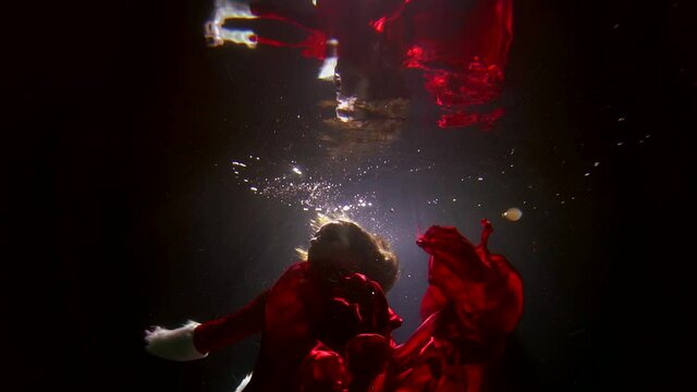lady in red is swimming underwater in pool, playing with swaying silk fabric, slow motion shot