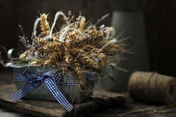 Still life with a bouquet of wheat ears and lavender in a metal pot on a wooden table.