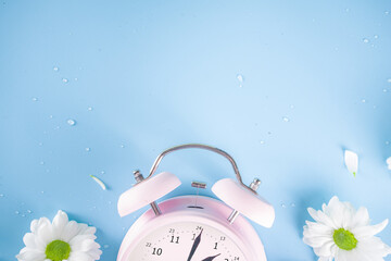 Spring Time Change flatlay. Summer back concept. Retro Vintage alarm Clock with fresh, beautiful white spring daisy flower on pastel blue background top view copy space