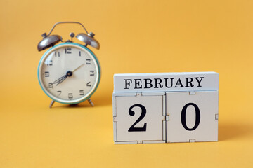  Calendar for February 20: cubes with the number 20 and the name of the month, alarm clock on a yellow background