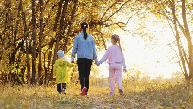 Mother and two children walking in the park and enjoying the beautiful autumn nature. Happy family on autumn walk.