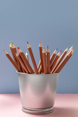 a set of colored pencils in a tin bucket on a pink and blue paper background. side view. a set for a young artist. the concept of children's creativity. selective focus