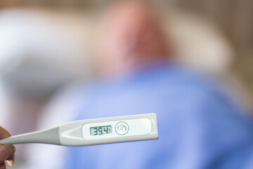 Persona de tercera edad al fondo y en primer plano un termómetro indicando alta temperatura