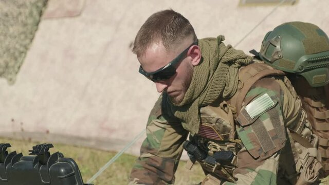Tilting-up closeup of military surveillance officer in camouflage clothing typing on laptop transmitting data on secret operation