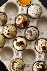 Quail eggs in the cardboard packing on the grey scratched table.