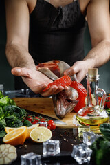 The big salmon is in the hands of the chef. He uses a knife to get the red caviar out of the fish.