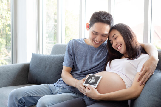 Happy pregnant woman and her husband holding and looking baby sonogram or ultrasound scan photo. First portrait of our baby. Concept of pregnancy, health care, gynecology, medicine.
