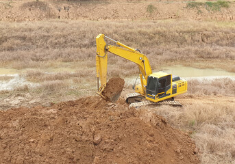 A yellow backhoe is digging a big pond. © Zblaster