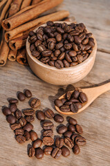 Coffee beans in the bowl and the top cinnamon sticks are placed on wooden table.
