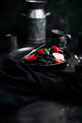 Black pasta with tomatoes and parmesan in a black plate