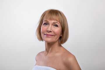 Fototapeta premium Aging gracefully. Beauty portrait of senior lady wearing towel, having silky skin, looking at camera on light background