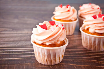 Valentines cupcakes cream cheese frosting decorated with heart shaped candy on the wooden background.