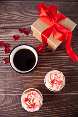 Valentines cupcakes cream cheese frosting decorated with heart candy, mug of coffee and gift box on the wooden background.