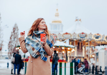 beautiful young woman in a felt hat and coat walking in the romantic city and drinking her coffee. street food at fair 