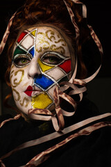 Carnival, a beautiful young woman with carnival makeup in the middle of a pandemic experiencing melancholy, black background, low key portrait, selective focus.