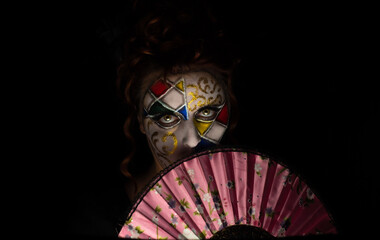 Carnival, a beautiful young woman with carnival makeup in the middle of a pandemic experiencing melancholy, black background, low key portrait, selective focus.
