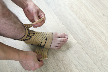 Fototapeta premium Human hands fix an elastic bandage sock to protect the ankle of the leg from sprains