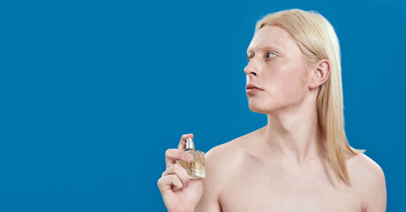 Young caucasian man holding perfume bottle near neck