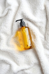 Yellow glass dispenser bottle with shower gel on white towel in bathroom. Natural organic SPA cosmetics. Flat lay, top view.