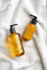 Yellow glass dispenser bottles on white towel. Natural organic SPA cosmetics. Flat lay, top view.