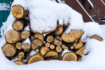 Oak logs stacked in a woodpile near the house as firewood for heating