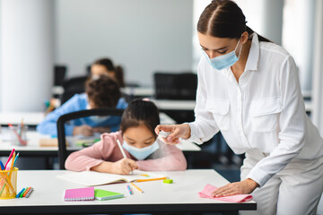 Teacher in mask cleaning desk with antibacterial sanitizer and napkin