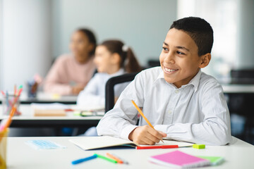 Portrait of small boy sitting at desk in classroom - Powered by Adobe