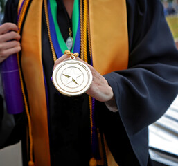 Proud graduate in graduation robe holds a gold medal.