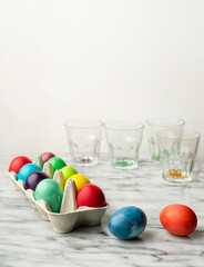 Colored Easter eggs in carton box on kitchen counter, emply glasses wirh remnants of dye