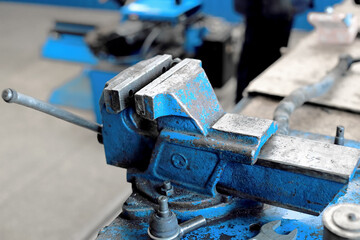 This is a large blue metal vise bolted to the workbench. An empty workplace in the workshop. The equipment for repair.