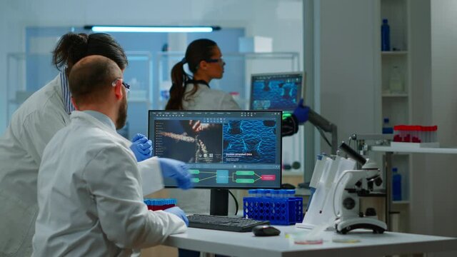 Group of scientists working in modern equipped laboratory pointing on computer desktop. Team of doctors examining vaccine evolution using high tech researching diagnosis against covid19 virus