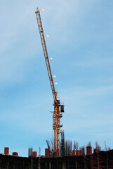 High yellow tower crane on a construction site of an urban building complex. On going high rise building without people against blue sky background.