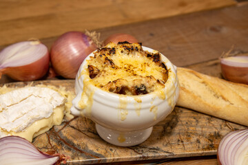 A delicious bowl of French Onion Soup with Camembert and a Cheddar Crust, surrounded with the ingredients used to create the dish on as wooden kitchen table