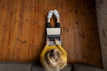Young female working on modern laptop sitting on floor at home. Top view