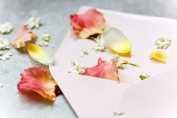 rosa, weiße und gelbe Blüten auf einem rosa Kuvert mit grau marmoriertem Untergrund als Detailaufnahme - Hochzeitseinladung, Papeterie, Deko