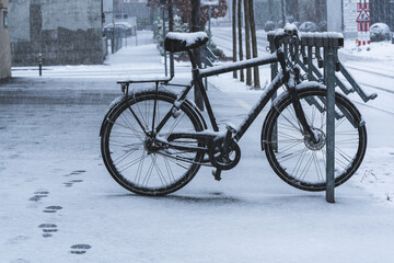 A snow-covered bike in a bike stand in the city. Footprints in the snow.