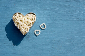 Celebration love concept: Top view on two little pearly hearts next to a big metallic heart filled with many small hearts on wooden blue background with copy space. For lovers and Valentines day