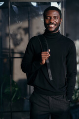 Student in black turtleneck with a backpack on his back smiling at the camera