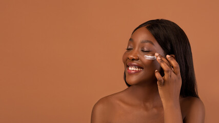 Delighted african american naked lady with eye cream