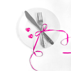 Fork and knife decorated with pink ribbon and decorative hearts on the plate on white. Table setting for Valentine's Day or wedding