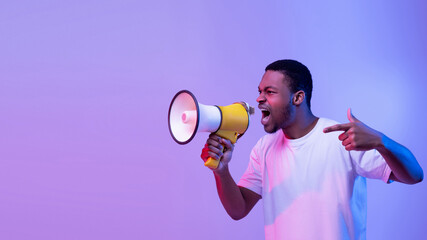 Full length portrait of aggressive young man shouting using megaphone isolated over purple studio wall, copyspace