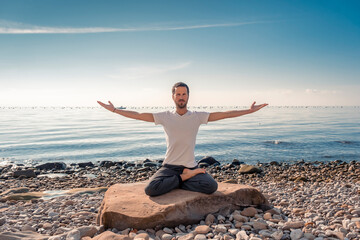 Attractive young man practicing yoga meditation and breathwork outdoors by the sea