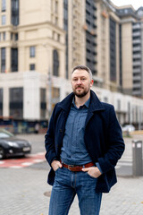 Fototapeta premium Trendy handsome man in gray coat and dark suit. Autumn city blurred background.