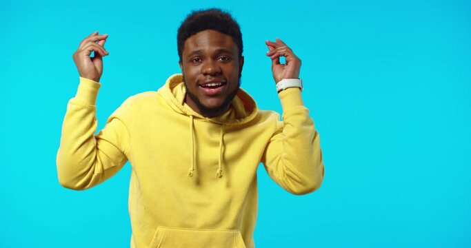 Close up portrait of happy joyful African American handsome young man dancing making funny rhythmic moves and gestures with hands isolated on blue background lin studio looking at camera, leisure