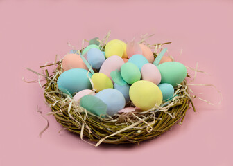 Multi-colored Easter eggs and feathers in pastel colors lie in a nest of branches on a pink background. Festive Easter card.