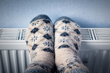 A man in woolen socks warms his frozen feet in winter on a home heating radiator.
