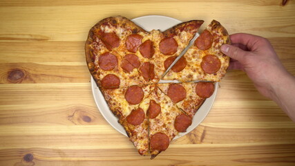 Heart shaped pizza for valentine's day. Young man takes a slice of pizza top view.