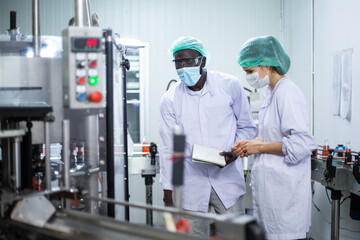 African American black man and woman worker inspecting drink product on bottling factory machinery. Process of beverage industrial concept. diversity people working together