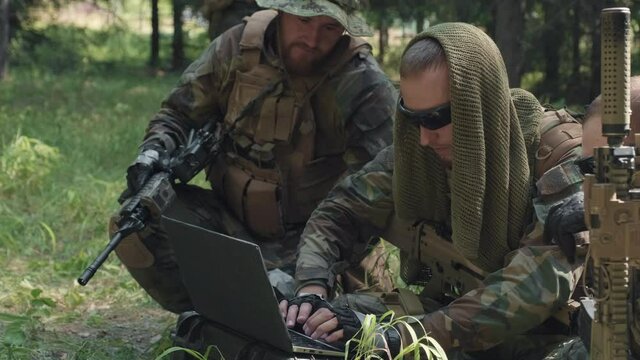 Medium shot of army officers in camouflage disguise using laptop, carrying out dangerous military operation in jungle